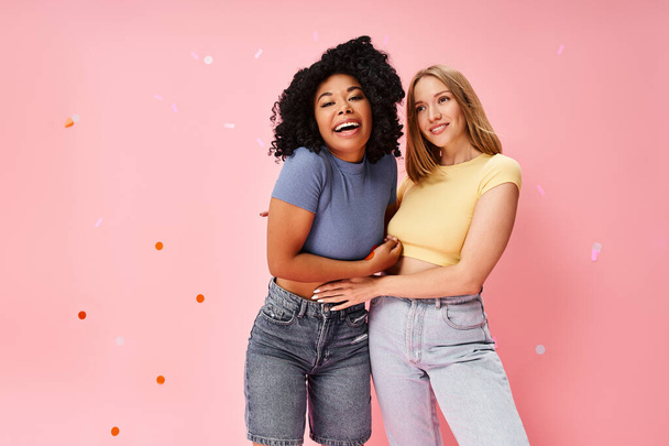 Two women in cozy casual attire standing together against a pink background. - Photo, Image