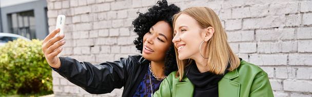 Dos atractivas mujeres diversas en atuendo casual tomando una selfie con un teléfono celular. - Foto, imagen