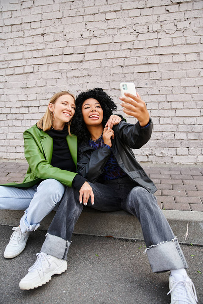 Due donne diverse in abbigliamento accogliente seduto a terra scattare una foto. - Foto, immagini