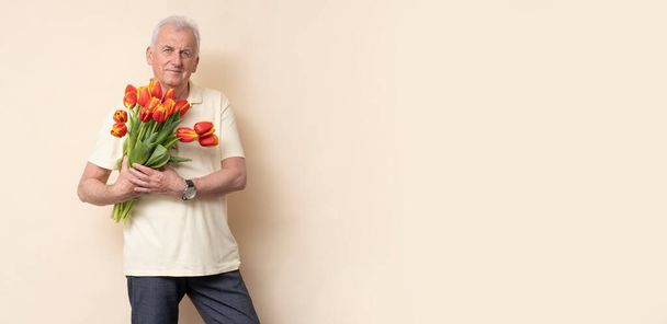 Jóképű idős férfi egy csokor tulipánnal a stúdióban.. - Fotó, kép