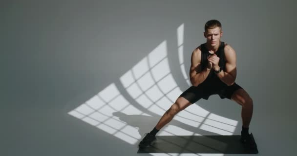 Sporty άνθρωπος σε activewear κάνει σωματική άσκηση σε στρώμα γιόγκα στο στούντιο με λευκό φόντο. Αθλητικός αρσενικό έχει προπόνηση και να κάνει πλευρική άσκηση lunge. Έννοια προθέρμανσης - Πλάνα, βίντεο