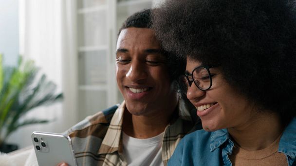 Afrikkalainen amerikkalainen pari mies ja nainen yhdessä kotona katsomalla puhelimen mobiililaitteella gadget Etsi tarjous valitsemalla tavaroita verkossa varaus lippuja loma keskustella perheen budjetti - Valokuva, kuva