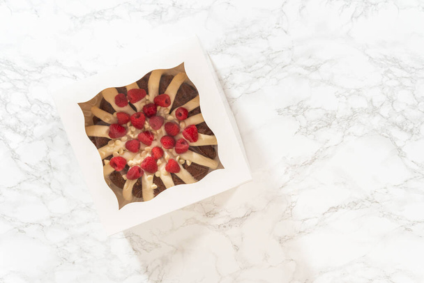 Litteä pano. Huolellisesti, White Chocolate Vadelma Bundt kakku on pakattu valkoiseen paperilaatikkoon valmiina lahjaksi tuomaan iloa ja hemmottelua jollekin erityiselle.. - Valokuva, kuva