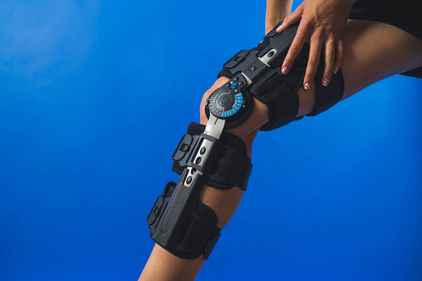 žena montáž kolenní výztuž s úhlem pohybu regulátor přes modré pozadí. Kvalitní fotografie - Fotografie, Obrázek