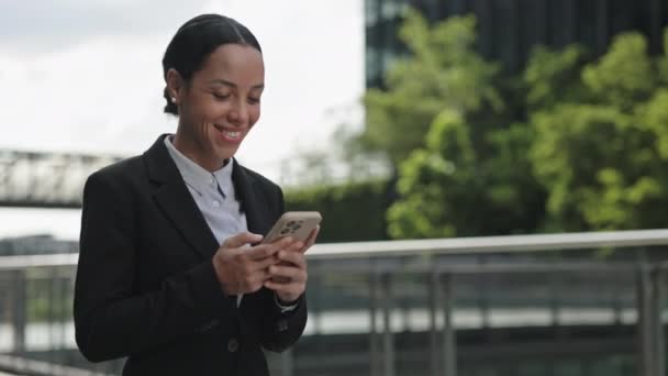 Sourire femme mignonne Consulting en ligne en utilisant Smartphone tout en marchant à l'extérieur. Jeune entrepreneur heureux Aller au centre d'affaires et bavarder en groupe de travail Chat - Séquence, vidéo