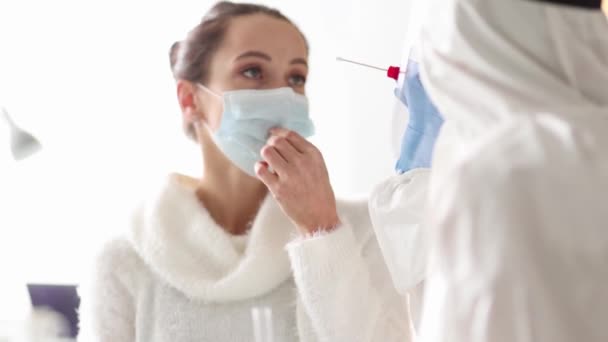 El médico con traje protector toma hisopo de la nariz de una mujer. Pruebas de laboratorio para el concepto de coronavirus - Imágenes, Vídeo