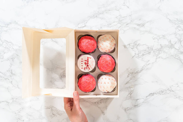 Flat lay. The birthday cupcakes, beautifully embellished with fondant decorations, are being carefully placed into white paper boxes, ready for their grand presentation. - Photo, Image