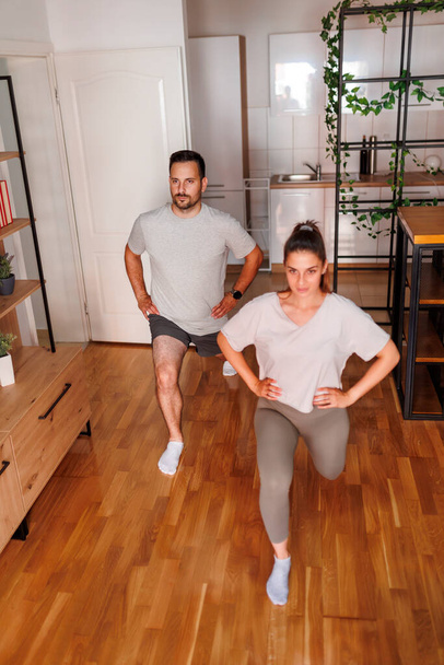 Active young couple working out together at home, doing lunges - 写真・画像