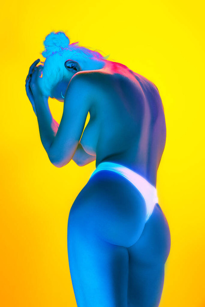 Rear view portrait of naked young woman in underwear in neon light against gradient background. Model with perfect body curves. Concept of art and femininity, female health, body care, self-love. - Photo, Image