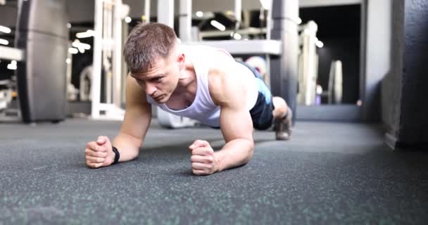 Man athlete with powerful biceps standing in plank on floor in gym 4k movie slow motion. Sport and health concept - Footage, Video