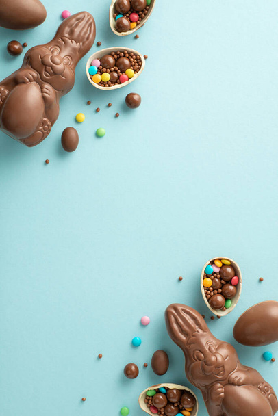 Joyful Easter selection motif. Directly overhead vertical shot of chocolate eggs cracked open, revealing colorful candies, a chocolate bunnies, sprinkles on a pastel blue ground, with space for text - Photo, Image