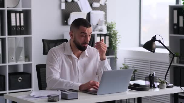 Boldogtalan kaukázusi üzletember, aki laptoppal dolgozik az asztalnál, és arccal a hivatalban. Munkahelyi stressz, pénzügyi kudarc, magas munkaterhelés. - Felvétel, videó