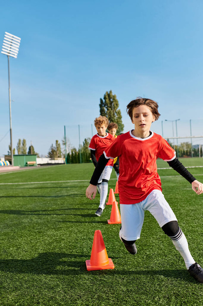 Ein fokussierter kleiner Junge kickt energisch einen Fußball um Kegel und demonstriert seine Beweglichkeit und Präzision bei der Ballkontrolle während einer Trainingseinheit. - Foto, Bild