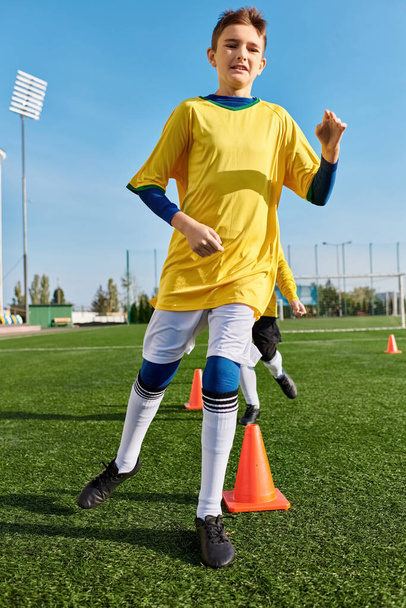 Ένα αγόρι με στολή ποδοσφαίρου κλωτσάει μια μπάλα ποδοσφαίρου με αποφασιστικότητα και ικανότητα σε ένα πράσινο πεδίο. - Φωτογραφία, εικόνα