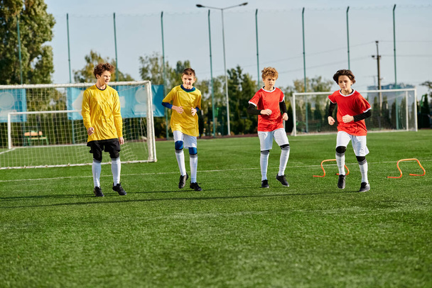 Żywa grupa młodych chłopców gra w piłkę nożną, kopiąc piłkę w tę i z powrotem z entuzjazmem na trawiastym polu. Są one ubrane w kolorowe koszulki i koncentrują się na strzelaniu goli podczas wyświetlania pracy zespołowej i umiejętności. - Zdjęcie, obraz