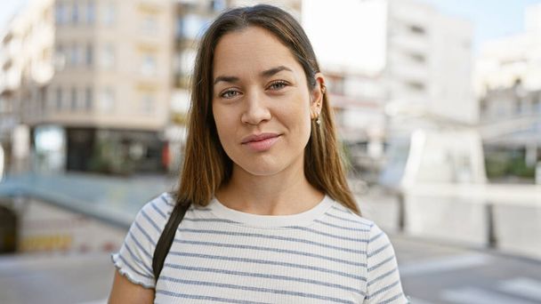 Portrait d'une jeune femme brune aux yeux bleus et aux cheveux longs dans une rue urbaine, reflétant un style de vie urbain. - Photo, image