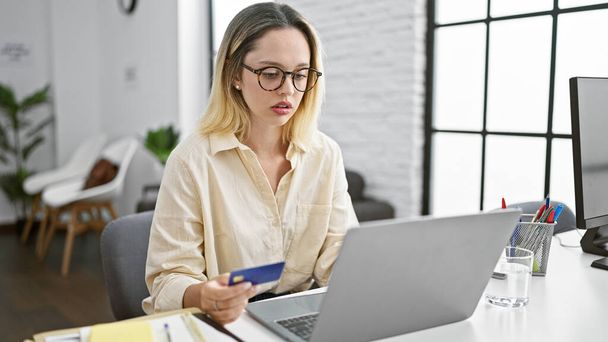Giovane donna bionda business worker shopping con laptop e carta di credito in ufficio - Foto, immagini