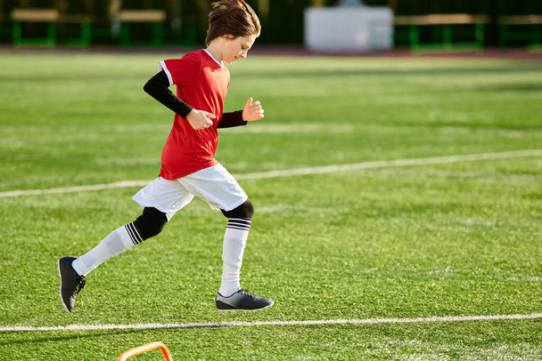 Динамичный молодой мальчик бежит по футбольному полю, сосредоточившись исключительно на предстоящей игре. С решимостью в глазах, он движется быстро и грациозно, демонстрируя свою ловкость и скорость. - Фото, изображение