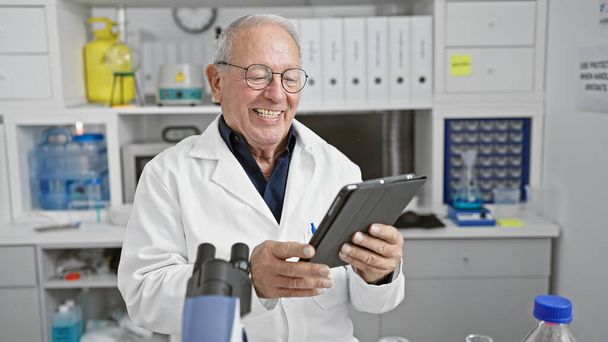 Hombre científico mayor sonriendo confiado usando touchpad en el laboratorio - Foto, imagen