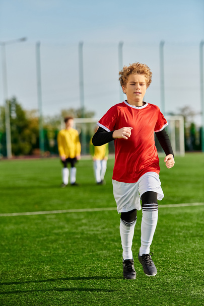 Un giovane ragazzo sta correndo gioiosamente attraverso un lussureggiante campo di calcio verde, con l'accento sul suo movimento agile e l'entusiasmo per il gioco.. - Foto, immagini