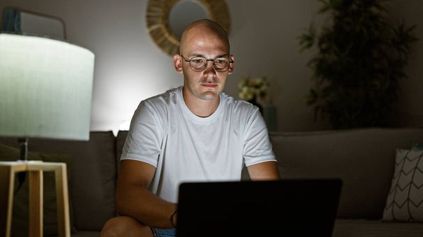 Hombre hispano joven usando portátil sentado en el sofá en casa - Foto, imagen