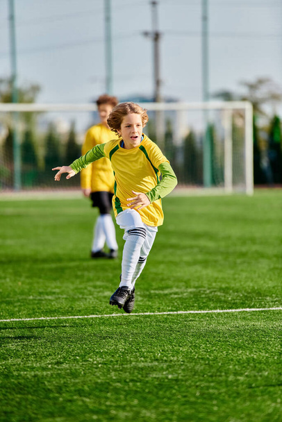 Ένα νεαρό κορίτσι με κίτρινη και πράσινη στολή ποδοσφαίρου κλωτσάει μια μπάλα ποδοσφαίρου με αποφασιστικότητα και επιδεξιότητα. - Φωτογραφία, εικόνα