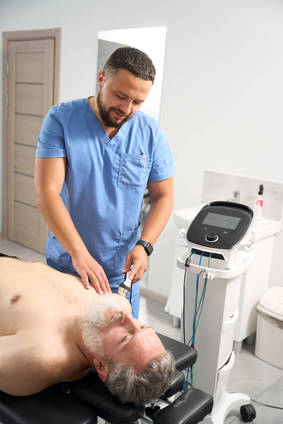 Fyzioterapeut lékař používá účinné léčebné metody pro pacienta, muž má šedé vousy - Fotografie, Obrázek