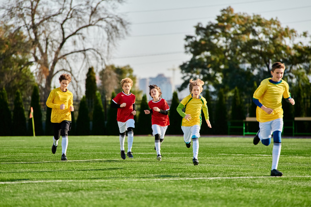 Een groep van diverse jonge kinderen, gekleed in kleurrijke truien, voetballen op een zonovergoten veld, schoppen tegen de bal, rennen en lachen in kameraadschap met gretige vastberadenheid. - Foto, afbeelding