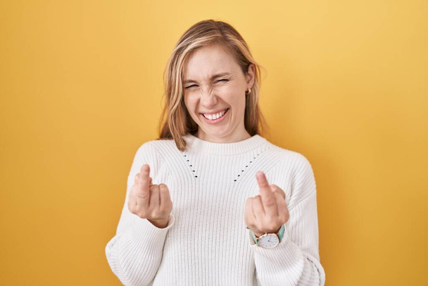 Young caucasian woman wearing white sweater over yellow background showing middle finger doing fuck you bad expression, provocation and rude attitude. screaming excited  - Fotó, kép