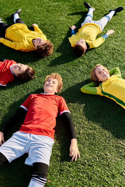 Group of young men laying comfortably on a vibrant green field, basking in the warmth of the sun. - Photo, Image