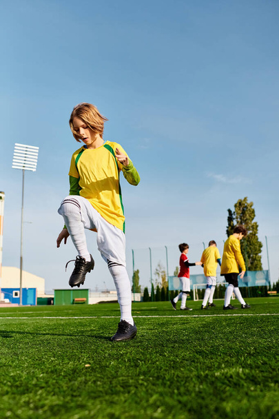 Młody chłopak z pasją kopie piłkę nożną na zielonym polu. Jego skoncentrowana ekspresja i umiejętne ruchy pokazują jego oddanie i miłość do sportu. - Zdjęcie, obraz