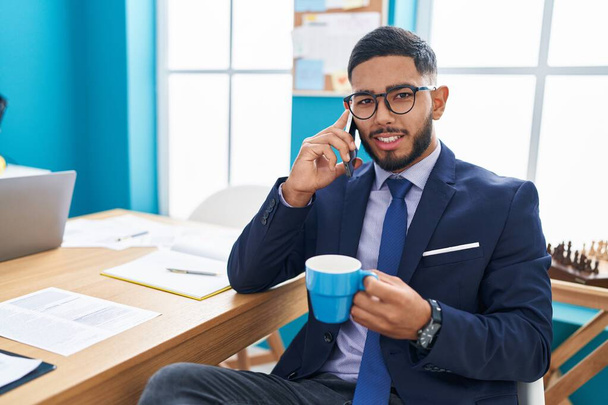 Trabajador de negocios joven latino hablando en smartphone bebiendo café en la oficina - Foto, imagen
