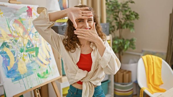 Впевнена, усміхнена молода жінка художник вражає фото позу руками в художній студії - Фото, зображення