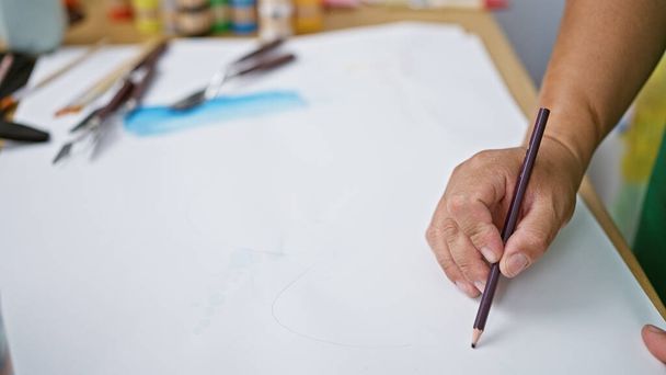 Παθιασμένος νεαρός Λατίνος καλλιτέχνης βυθισμένος στο σχέδιο στο σημειωματάριό του, τοποθετημένος στην καρδιά ενός ζωντανού στούντιο τέχνης - Φωτογραφία, εικόνα