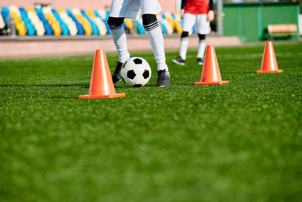 Zkušený fotbalista obratně kopne fotbalový míček přes řadu oranžových kuželů nastavených ve výcvikovém cvičení. Hráči se zaměřují, agility, a ovládání jsou zřejmé, jak navigovat kurz s obratností. - Fotografie, Obrázek