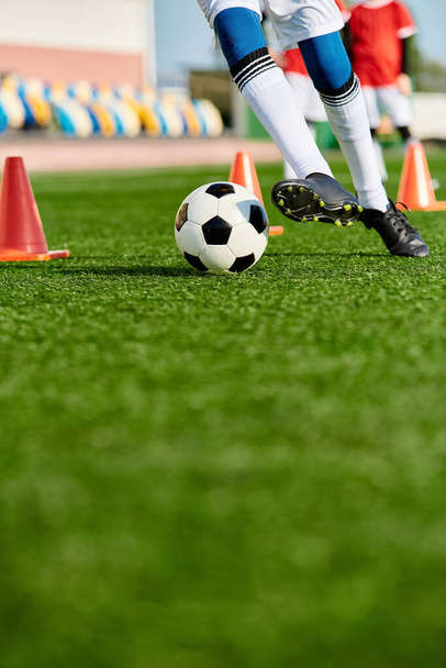 Una persona que usa equipo deportivo está pateando una pelota de fútbol en un campo verde bajo un cielo azul claro en un día soleado. - Foto, Imagen