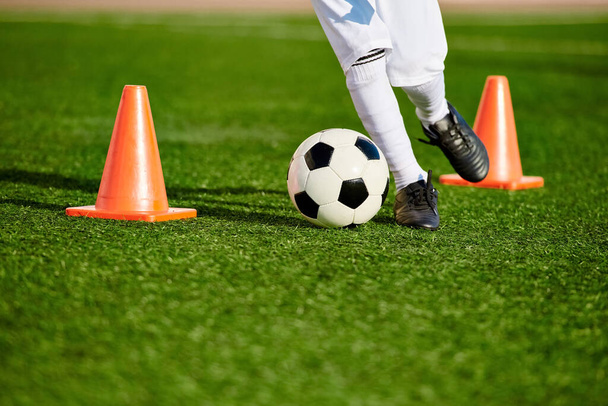 Een persoon die voetbalvaardigheden toont door een bal rond oranje kegels te schoppen op een veld. Het individu is gefocust en wendbaar, toont precisie en controle. - Foto, afbeelding