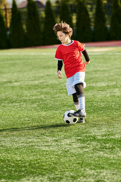 Genç bir çocuk canlı bir sahada güvenli bir şekilde bir futbol topunu tekmelerken görülüyor. Odaklanmış ve kararlı, spor için yetenek ve tutku sergiliyor.. - Fotoğraf, Görsel