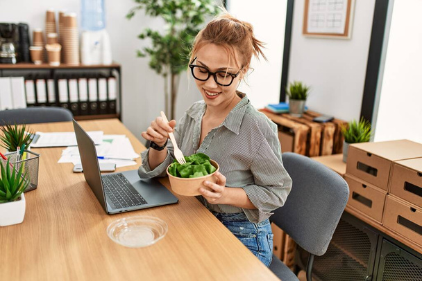 Young caucasian woman business worker using laptop eating salad at office - Foto, Imagem
