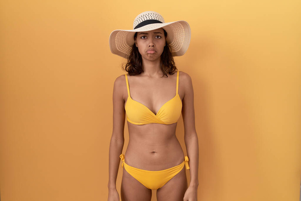 Jeune femme hispanique portant un bikini et un chapeau d'été déprimée et inquiète pour la détresse, pleurant en colère et effrayée. triste expression.  - Photo, image