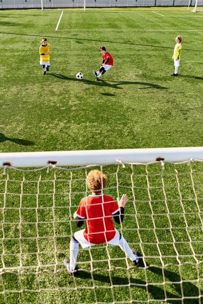Μια ομάδα μικρών παιδιών, γεμάτη ενέργεια και ενθουσιασμό, που παίζουν ένα συναρπαστικό παιχνίδι ποδοσφαίρου. Τρέχουν, κλωτσώντας την μπάλα, και ζητωκραυγάζουν ο ένας τον άλλον καθώς συμμετέχουν σε φιλικό ανταγωνισμό στο γήπεδο. - Φωτογραφία, εικόνα