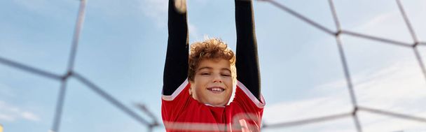 Neşeli genç bir çocuk renkli bir voleybol ağında baş aşağı asılı duruyor. Maceracı ruhunu ve eşsiz aktivitelere olan sevgisini sergiliyor.. - Fotoğraf, Görsel
