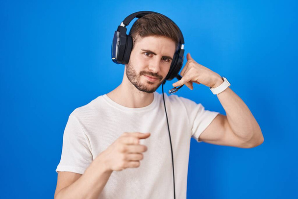 Іспаномовний чоловік з бородою слухає музику в навушниках, посміхаючись розмовляти по телефону жестом і вказуючи на вас. зателефонуй мені.  - Фото, зображення