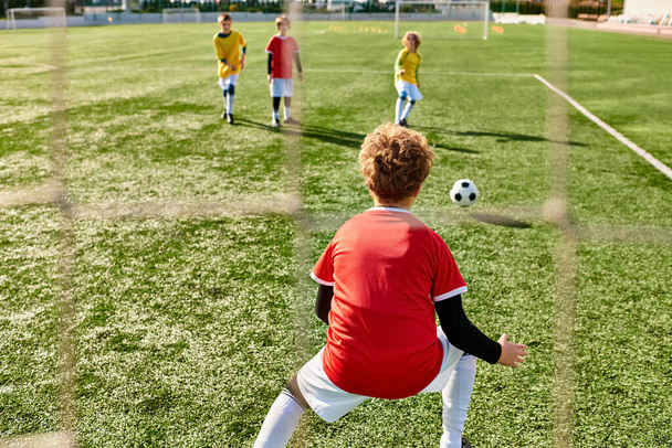 Eine Gruppe kleiner Kinder spielt energisch Fußball, rennt, tritt und gibt den Ball auf der grünen Wiese weiter. - Foto, Bild