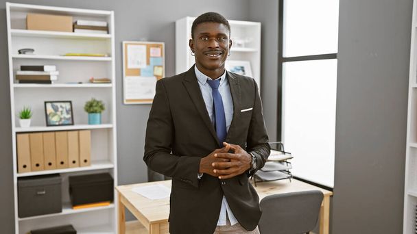Впевнений африканський бізнесмен стоїть в сучасному офісі, виглядає професійно і красиво - Фото, зображення