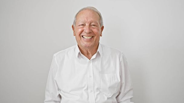 Απλό στιγμιότυπο ενός χαρούμενου, χαμογελαστού ηλικιωμένου άντρα, γεμάτο αυτοπεποίθηση και χαρά, να στέκεται σε ένα απομονωμένο λευκό φόντο, ακτινοβολώντας ευτυχία στον ώριμο τρόπο ζωής του.. - Φωτογραφία, εικόνα
