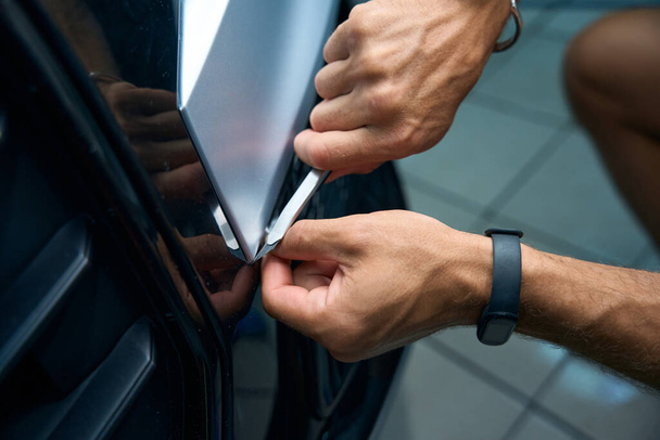 A férfi óvatosan levágja a felesleges kavicsellenes fóliát az autó karosszériáján, éles kést használ. - Fotó, kép