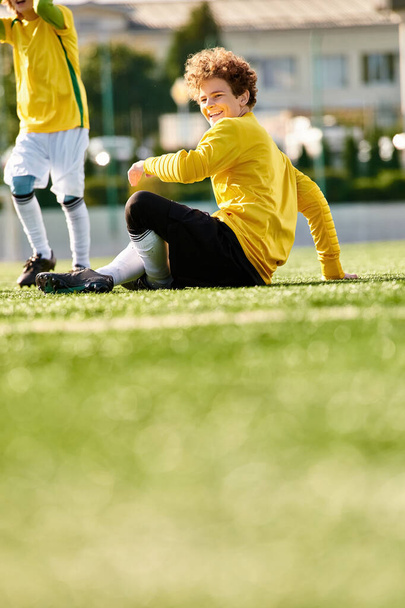 Ένας νεαρός που απολαμβάνει μια στιγμή περισυλλογής ενώ κάθεται στο έδαφος δίπλα σε μια μπάλα ποδοσφαίρου.. - Φωτογραφία, εικόνα