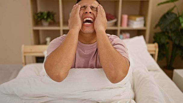Besorgter junger lateinischer Mann schreit in Schlafzimmerruhezone, lautere Sorge hallt von den Wänden in seiner Wohnung wider - Foto, Bild
