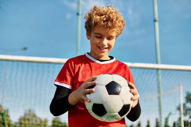 Młody chłopak stoi przed bramką, trzymając piłkę. Wygląda na skupionego i zdeterminowanego, gotowego strzelić gola. Scena oddaje istotę pasji i emocji dla sportu piłki nożnej. - Zdjęcie, obraz